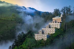 Luxury hotel perched on misty mountain ridge surrounded by tea plantations and forest