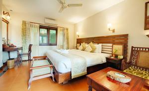 Spacious bedroom with wooden bed frame, terracotta floor, and garden view windows