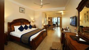 Spacious luxury suite with carved wooden bed, navy pillows, and adjoining living area with sea view